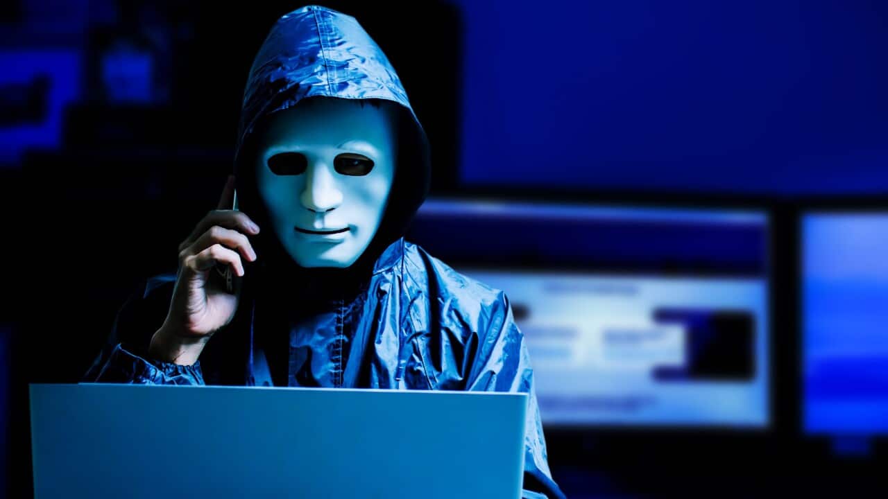 A Male Hacker Wearing Mask While Using Laptop At Table In Darkroom