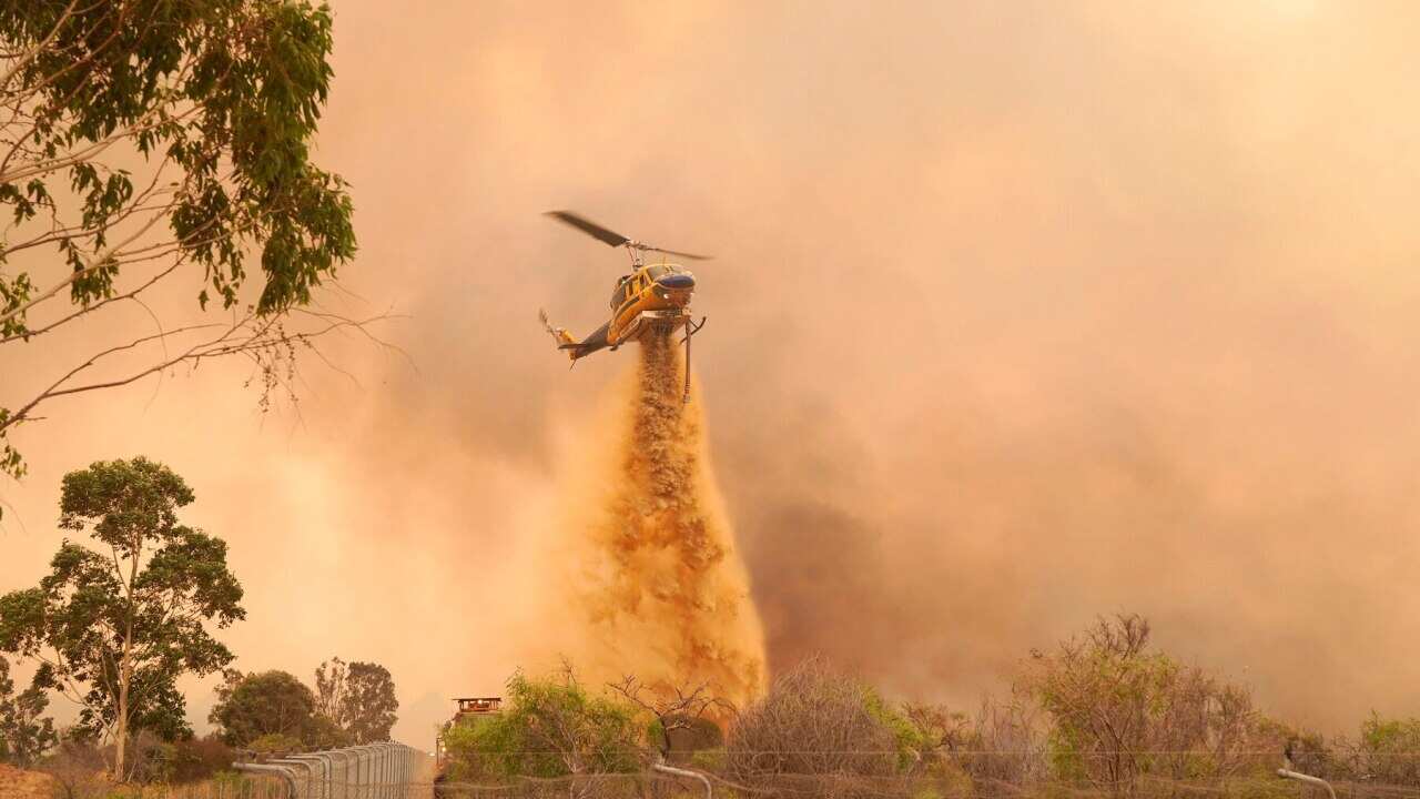 A helicopter drops fire retardant on a fire near Wooroloo