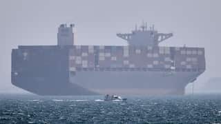A container ship on the ocean, a smaller boat is in the foreground