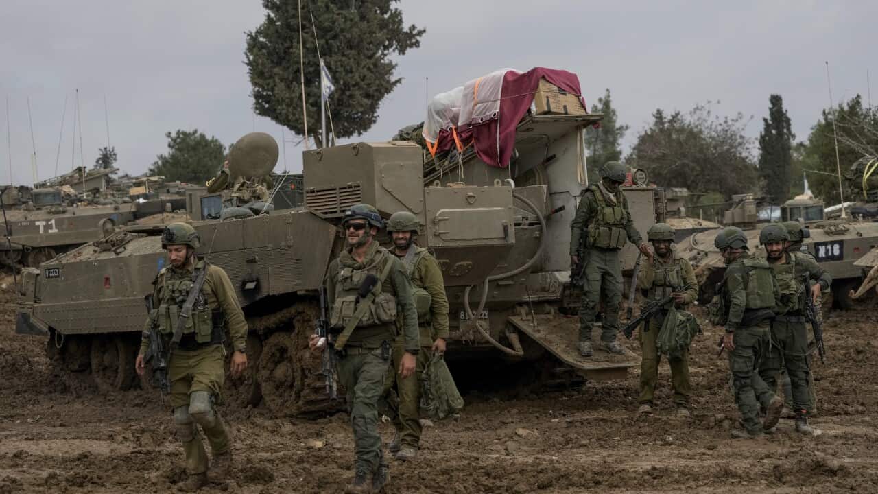 Soldiers standing near tanks which are parked on a muddy road.