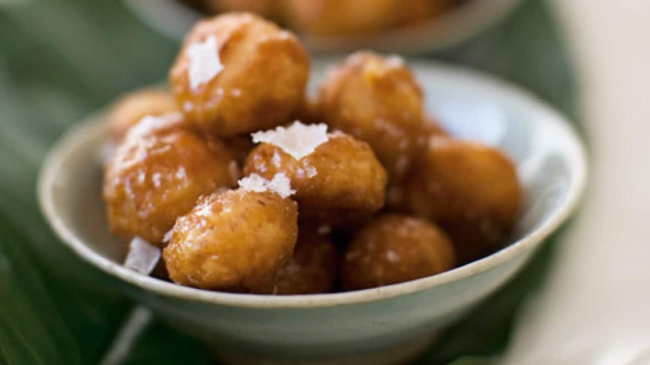 Toffee macadamias sit in a small bowl, with a few flakes of salt on top.