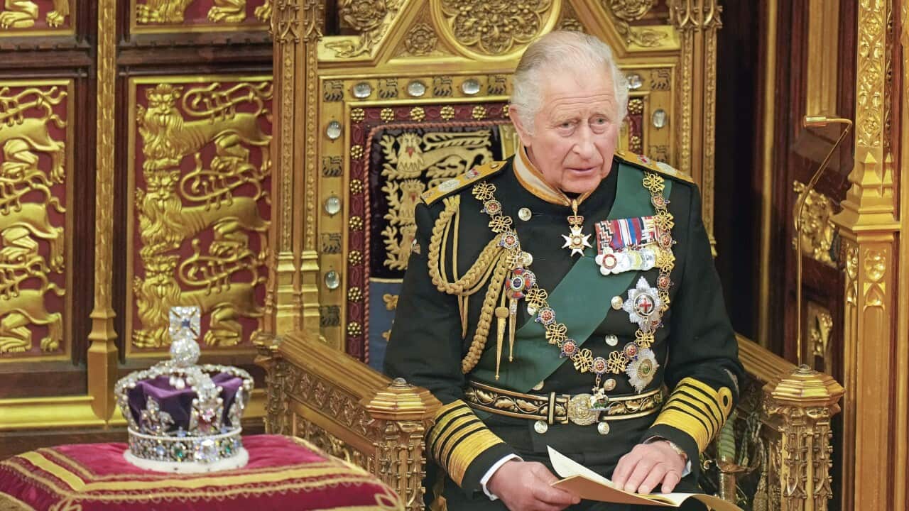 The then-Prince of Wales sitting on a throne next to the Imperial State Crown.