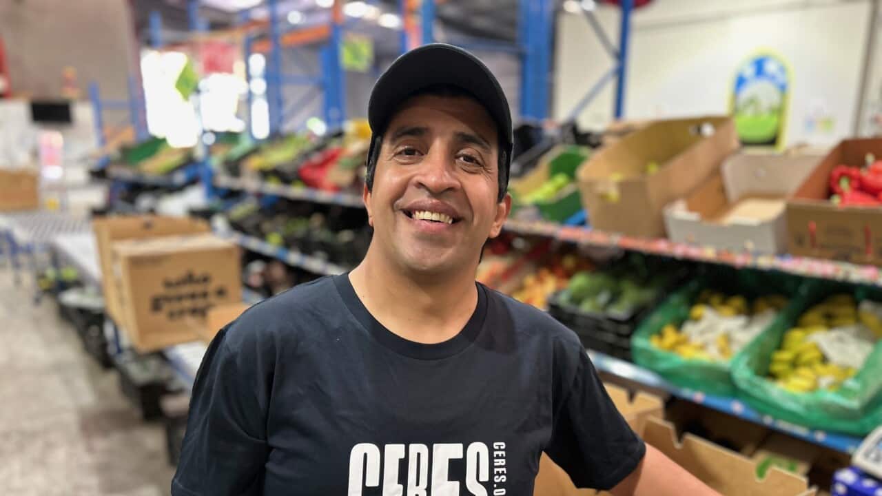 A man in a black t-shirt leaning on cardboard boxes in a warehouse.
