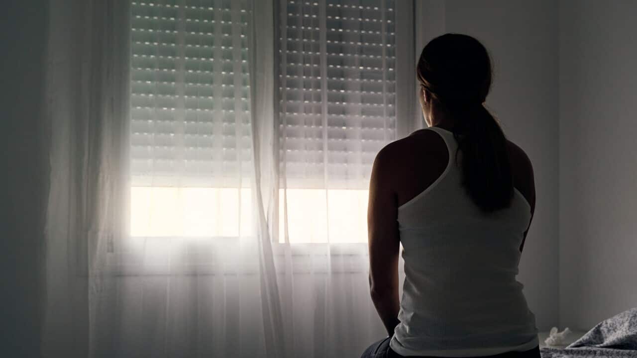 Rear view of an unrecognisable woman sitting on her bed looking out the window.