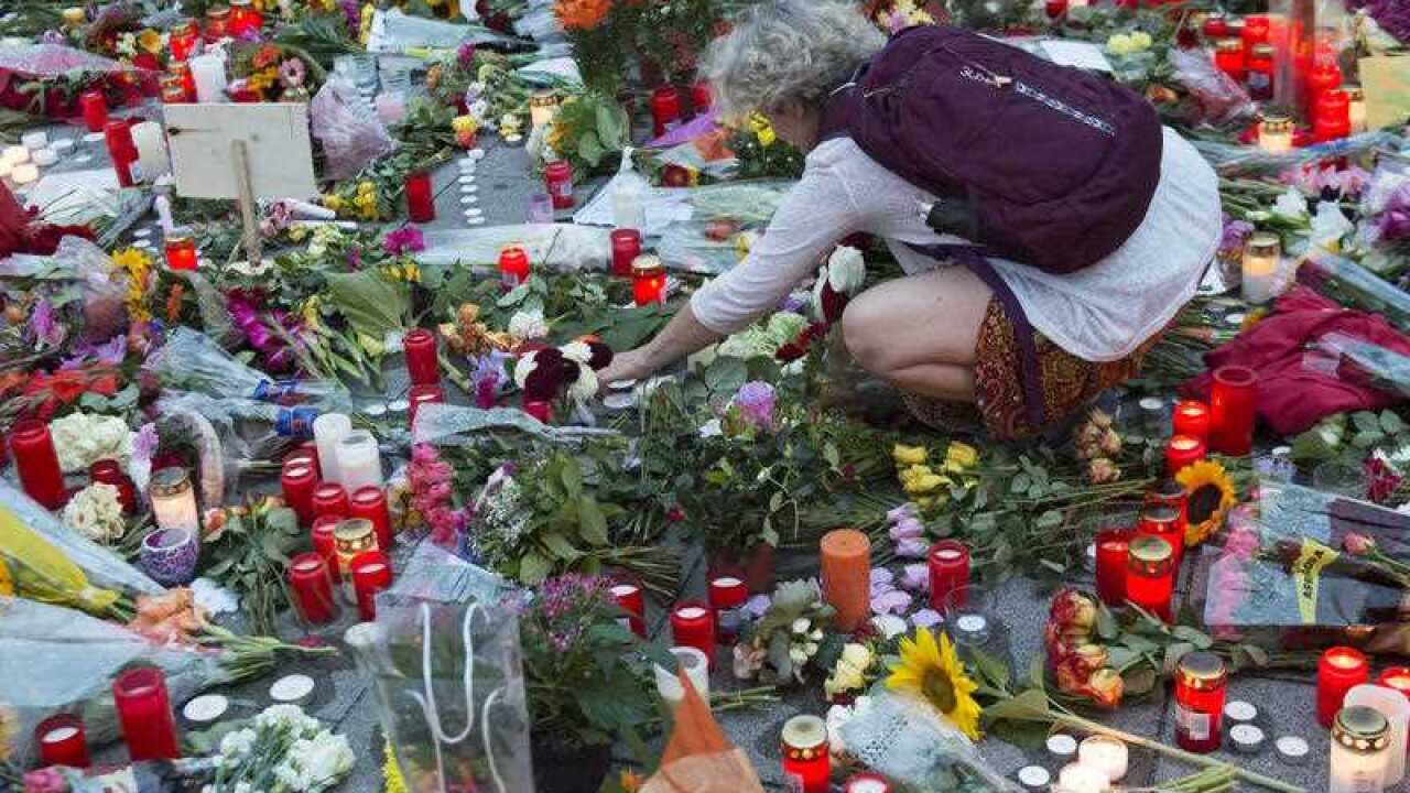 A woman adjusts a candle among flower tributes near to the Olympia shopping center