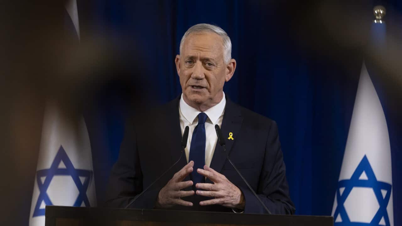A man in a suit standing in front of two Israeli flags