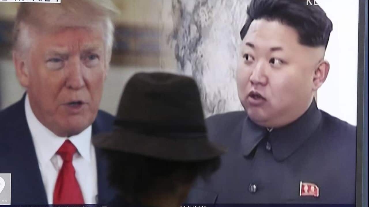 A man paases a television showing Donald Trum and Kim Jong Un