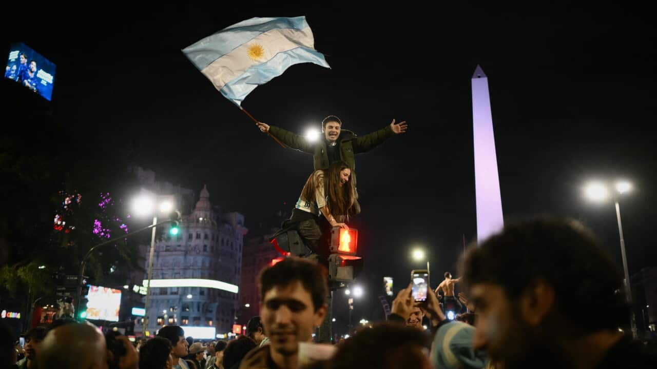 Argentinian fans wave a national flag in a city square at night.