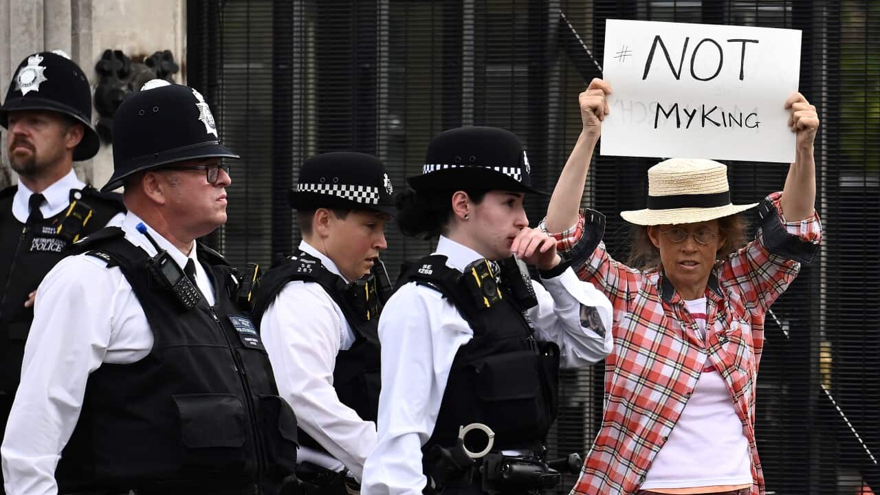A woman with a sign reading"not my king" is escorted by police