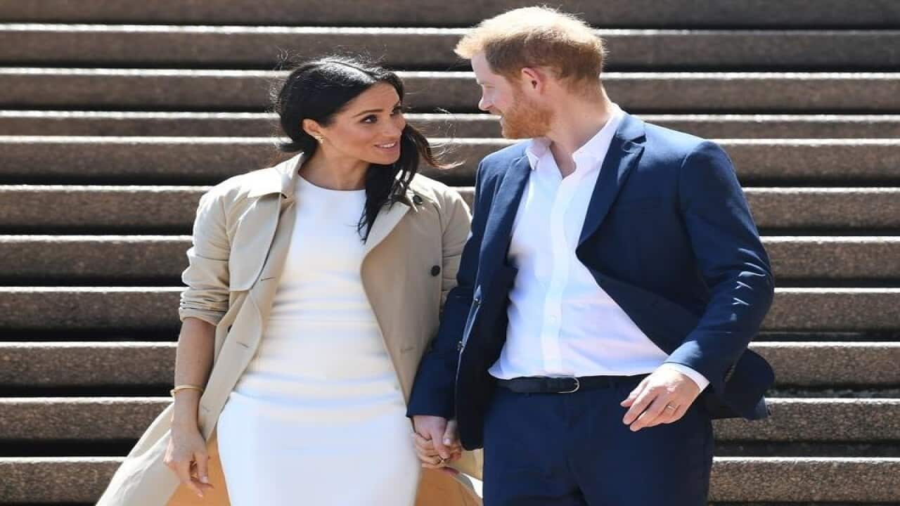 Britain's Prince Harry, and wife Meghan walk down stairs.