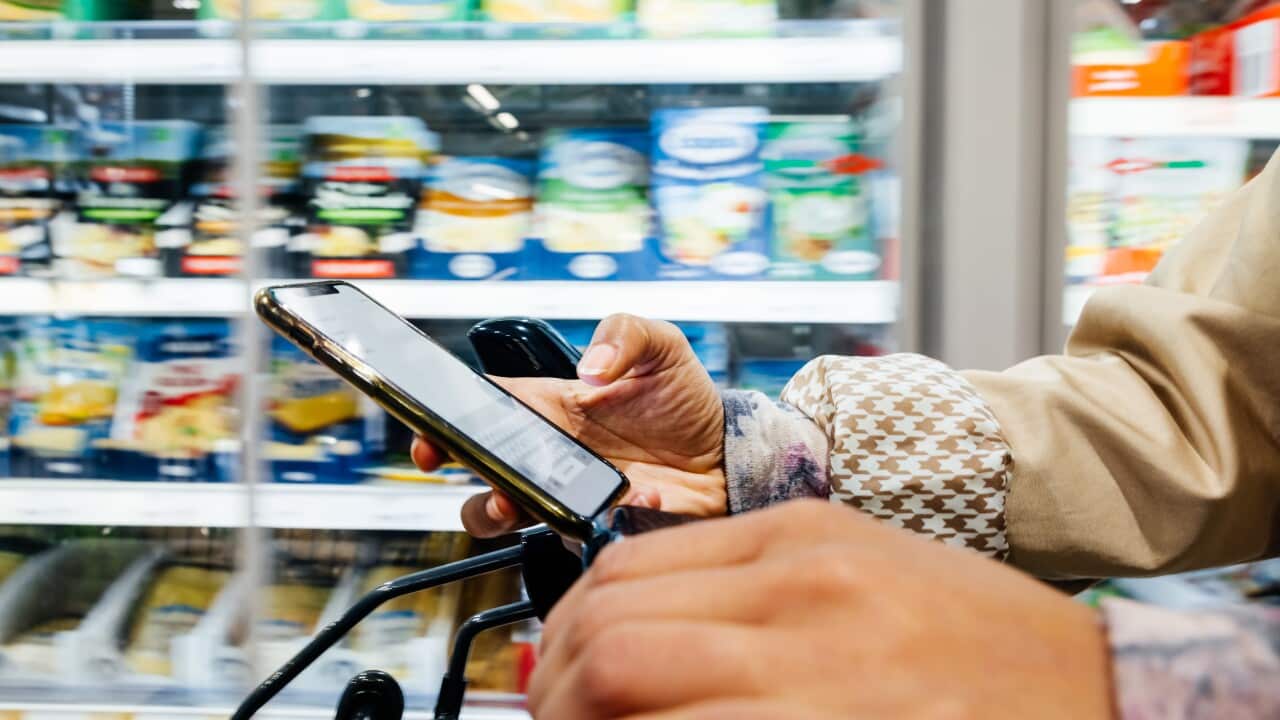 Close-up of woman using smartphone while pushing trolley.