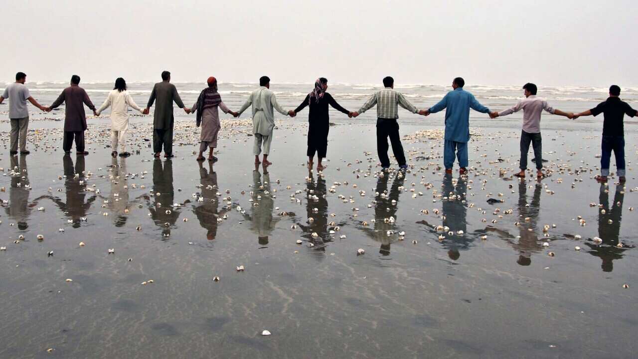 People make a hand chain at the beach as the Navy recovers bodies of those drowned