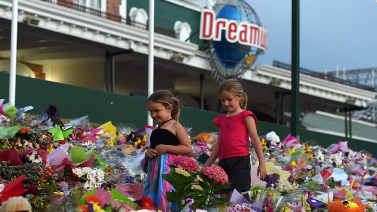 Young girls walk through floral tributes outside Dreamworld