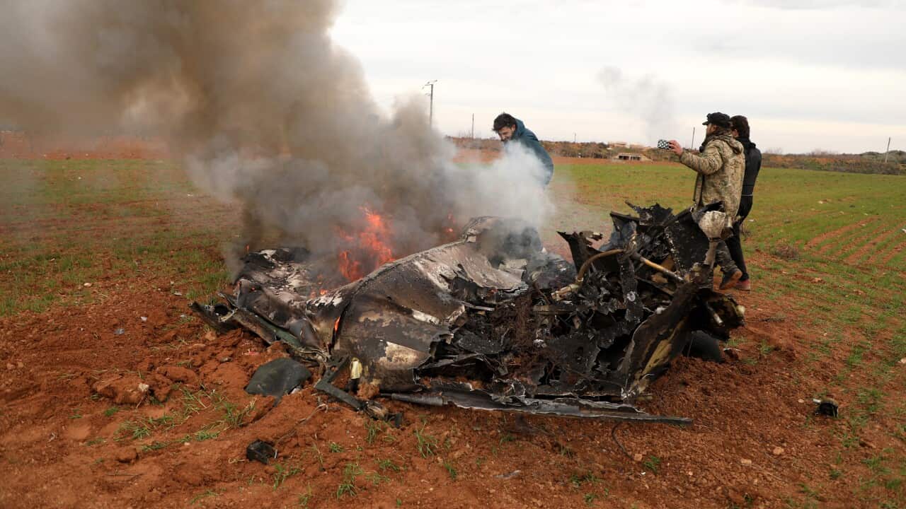 Armed men stand next to the burning remains of an alleged Syrian army helicopter that was shot down in the village of Qaminas