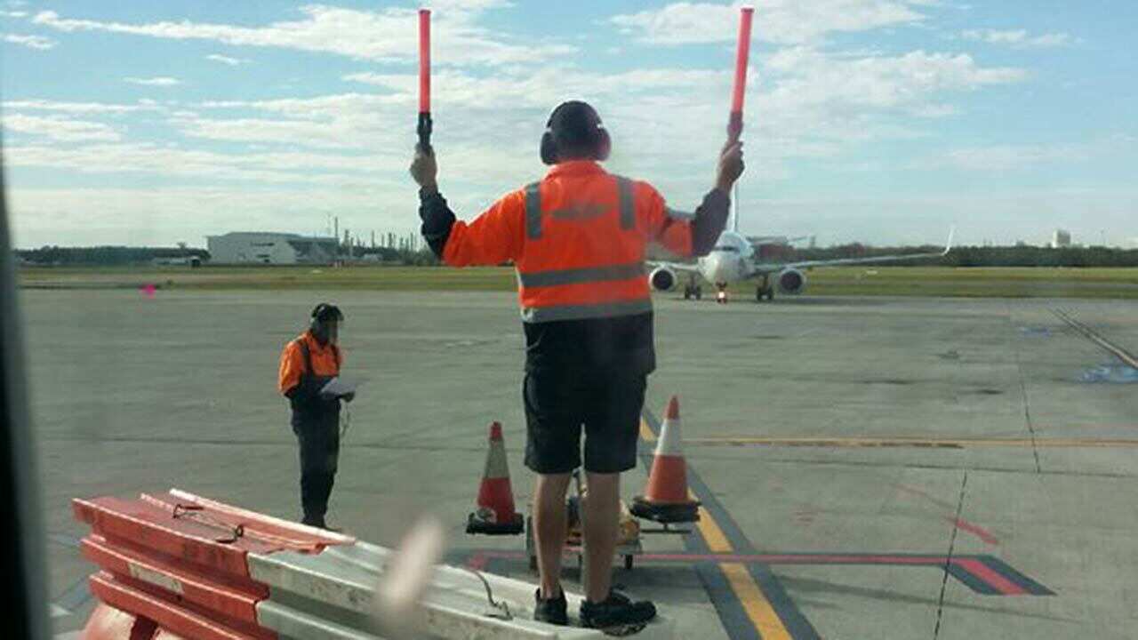 TWU picture shows an Aerocare worker standing on bollards to direct a plane.