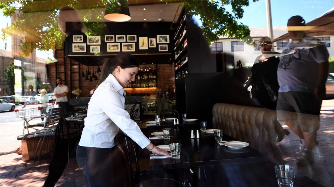 A hospitality worker sets down cutlery at a table.
