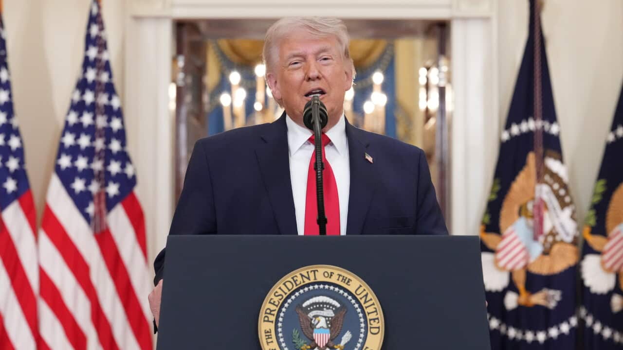 Donald Trump standing at a podium bearing the US president's seal.