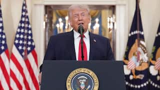 Donald Trump standing at a podium bearing the US president's seal.