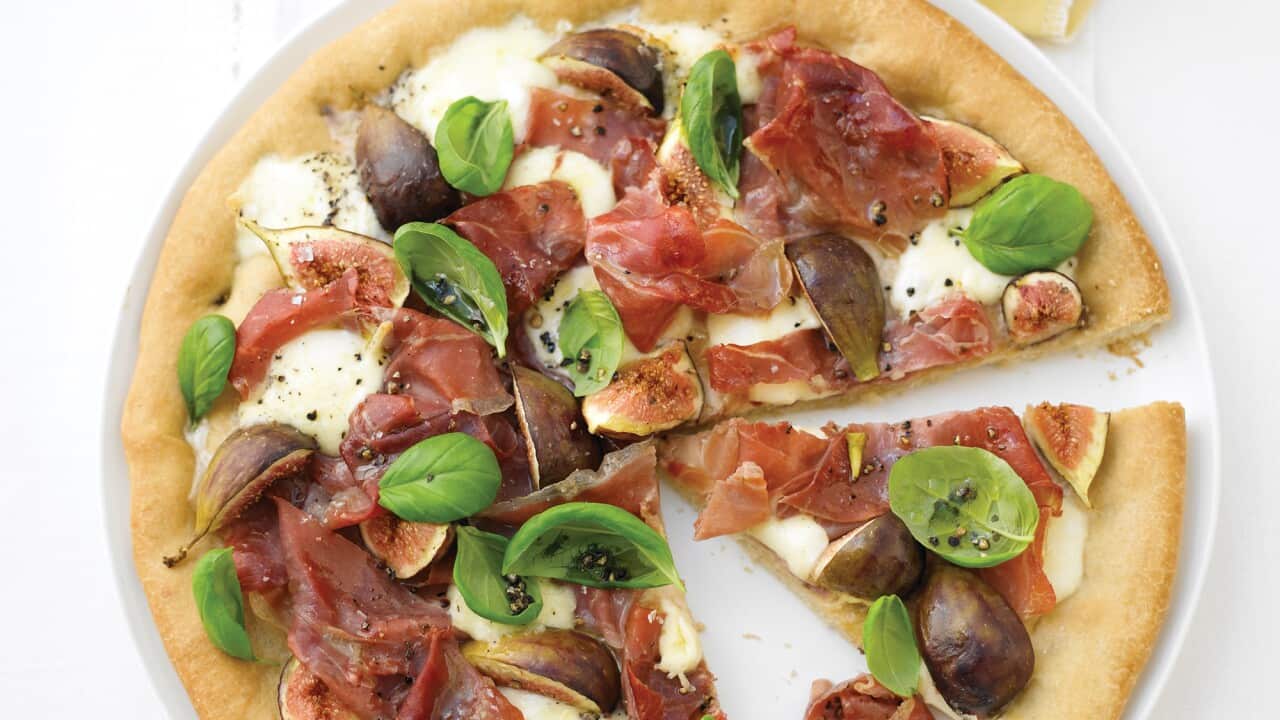 A fig and proscuitto pizza, sitting on a white plate, is seen from overhead.