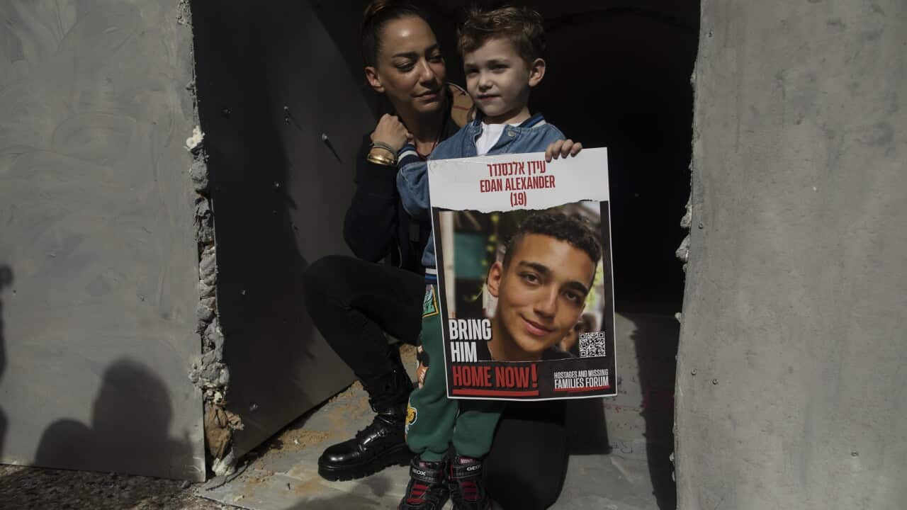 A child is holding a poster of a man with a woman crouched behind him.