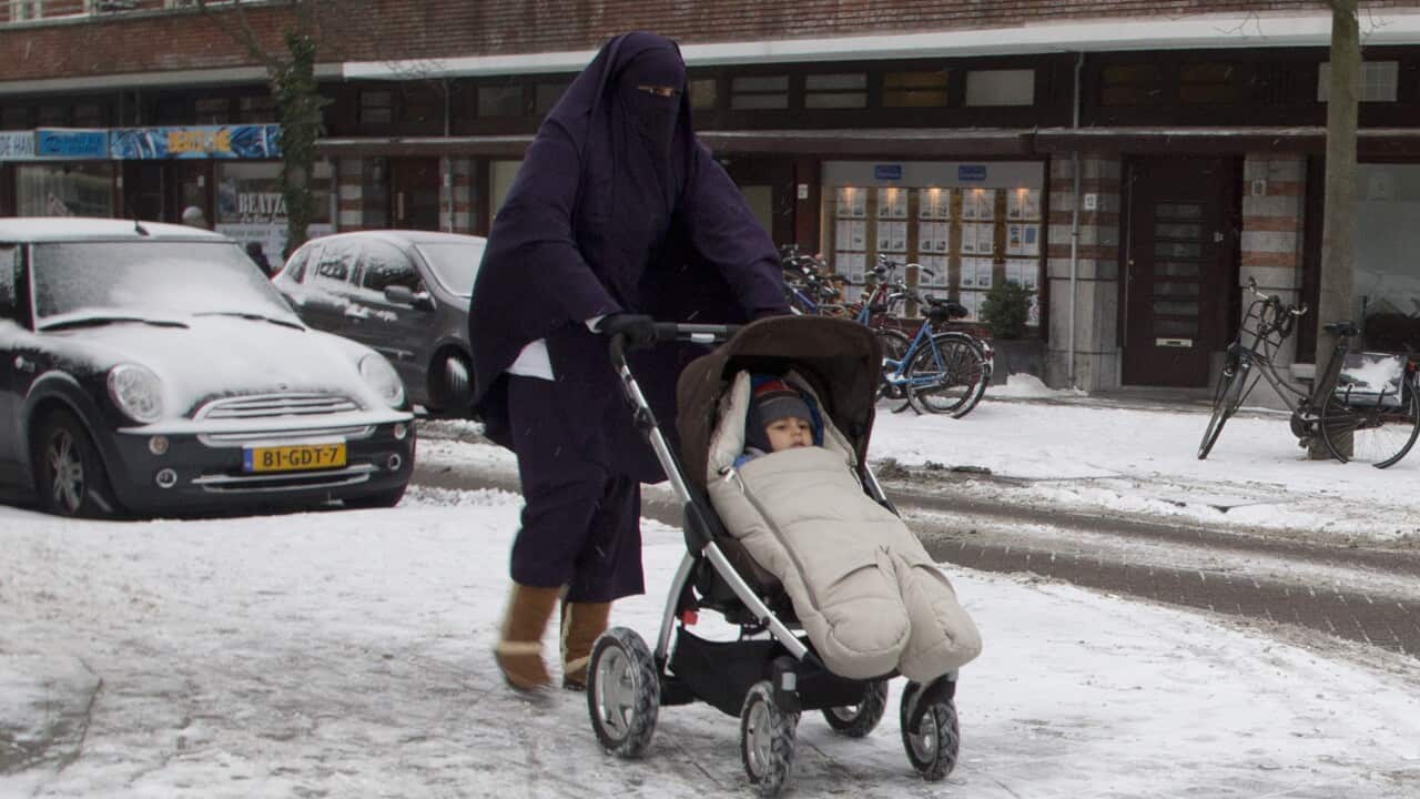 A woman wearing a niqab pushes a baby stroller on snow-covered streets in Amsterdam.