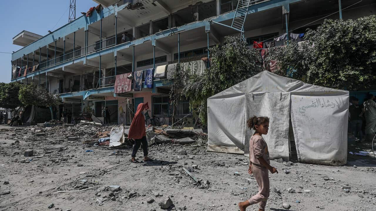 An adult and young girl walk past a building that has been damaged by an airstrike.