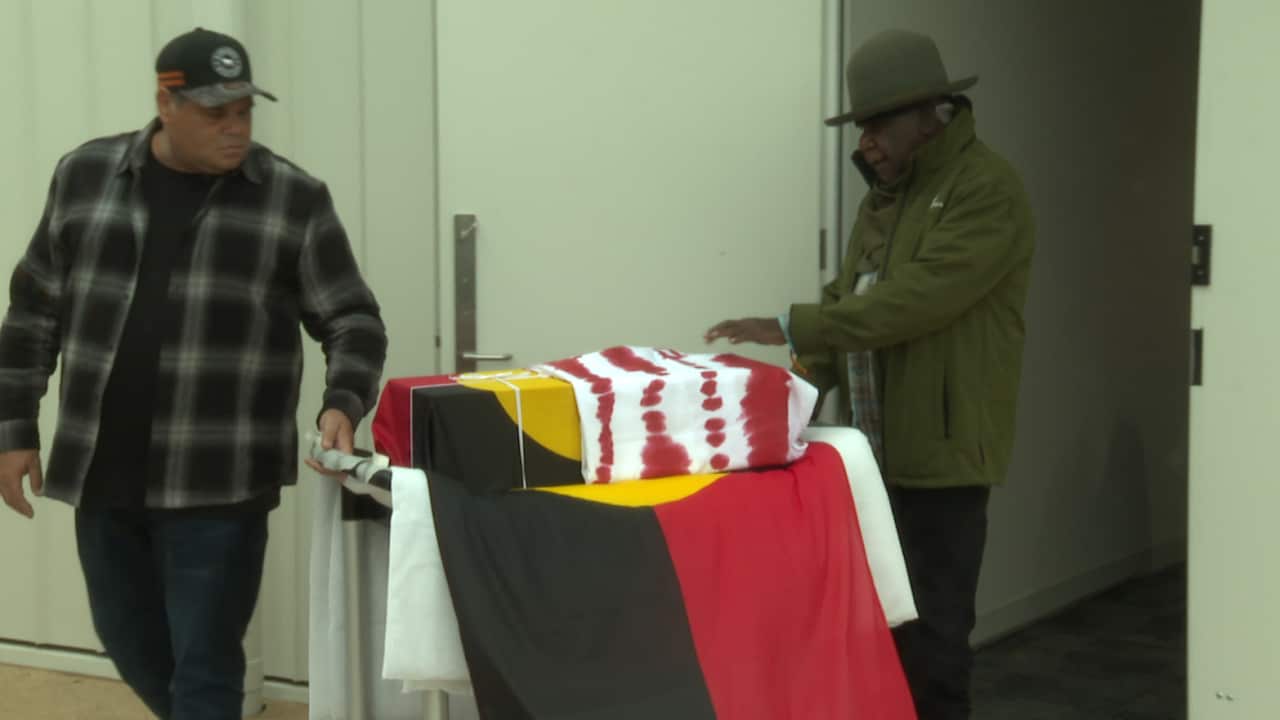 Two men stand over a box covered in an Aboriginal flag.