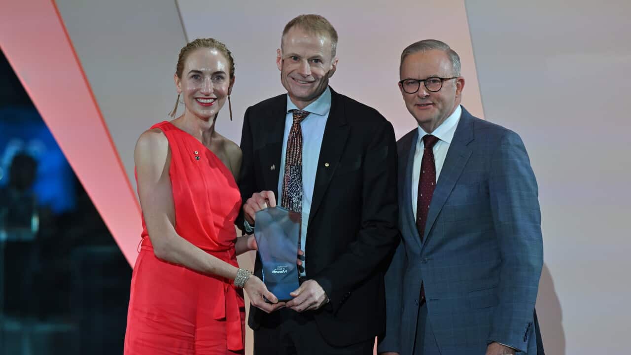A woman in a red dress and a man in a suit hold and award while posing with Prime Minister Anthony Albanese