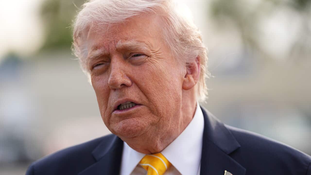 Trump sitting at his desk in the Oval Office at the White House wearing a navy suit and a red tie