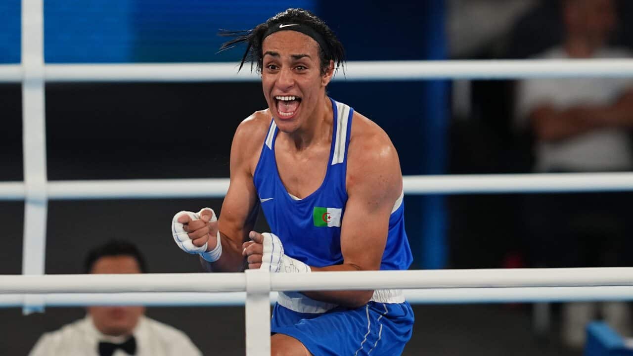 Imane Khelif, wearing a blue singlet and shorts, celebrates while in the boxing ring.