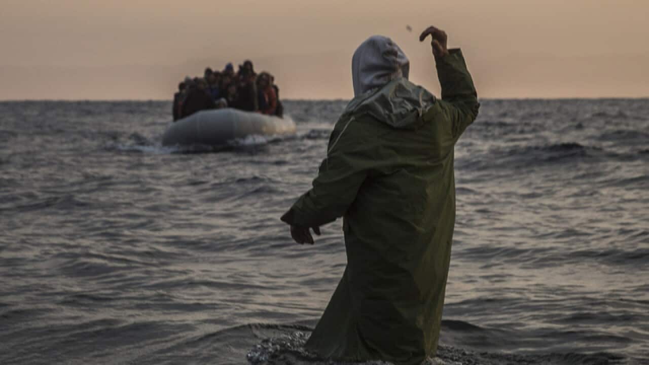 A volunteer gestures to refugees and migrants aboard a dinghy