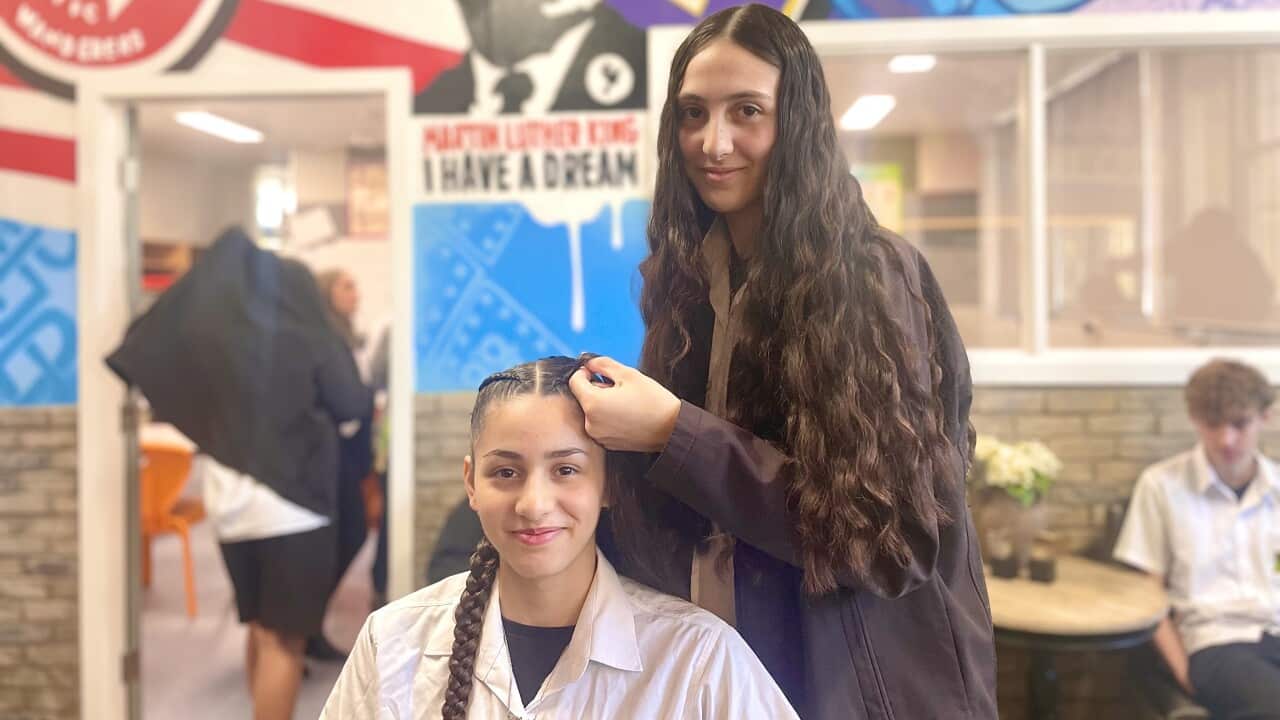 A girl braids her friend's hair in a hair salon with colourful murals.