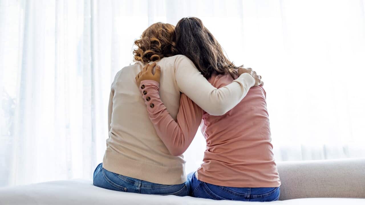 Rear view of mother and daughter embracing sitting on bed