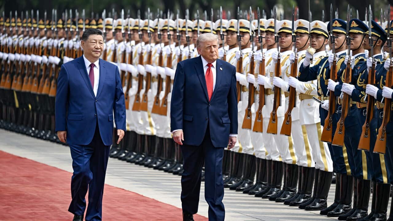 An older white man and an older asian man walking past soldiers in formation