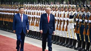 An older white man and an older asian man walking past soldiers in formation