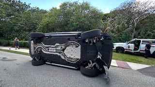 A dark SUV lying completely on its side in the middle of a paved road after an accident.