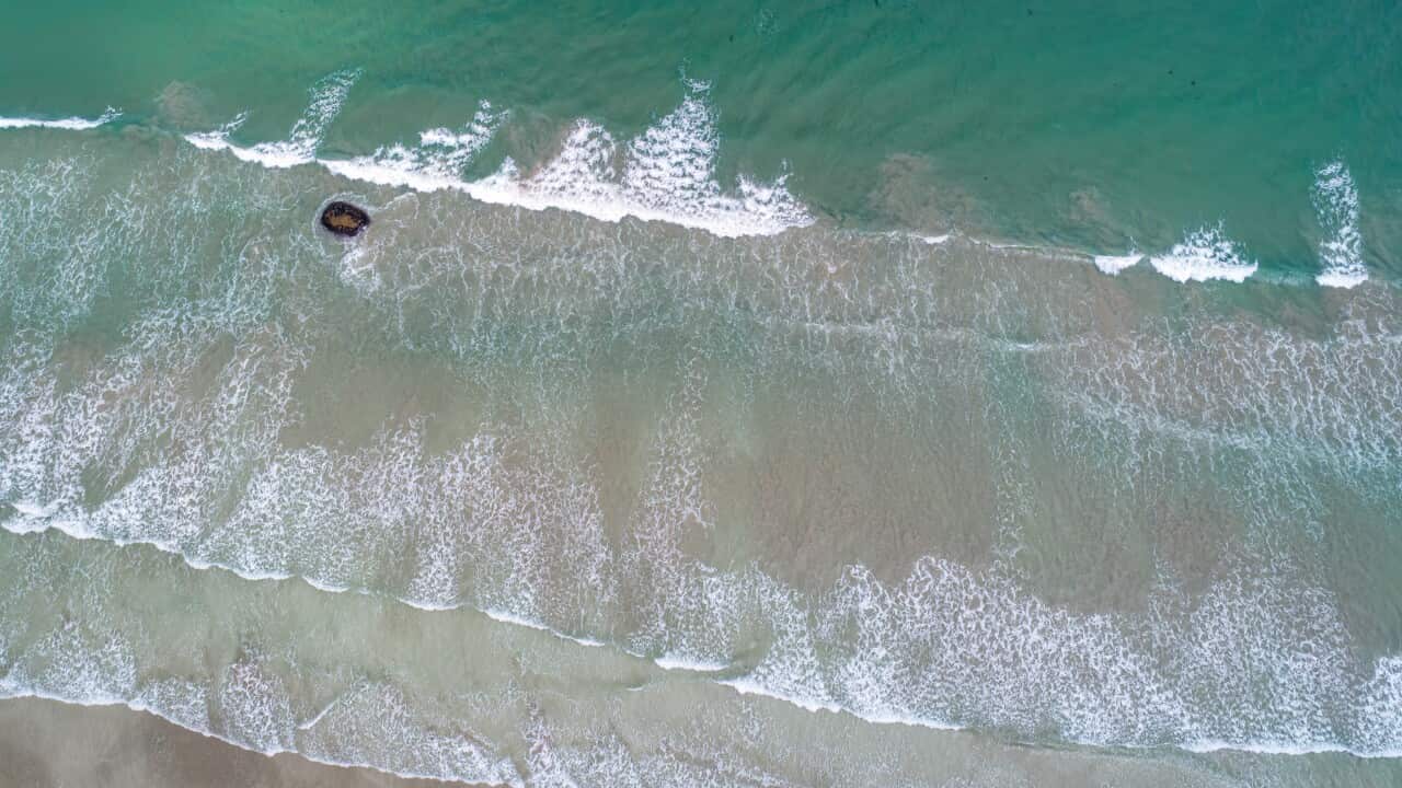 An overhead shot shows waves crashing on a sandy beach.