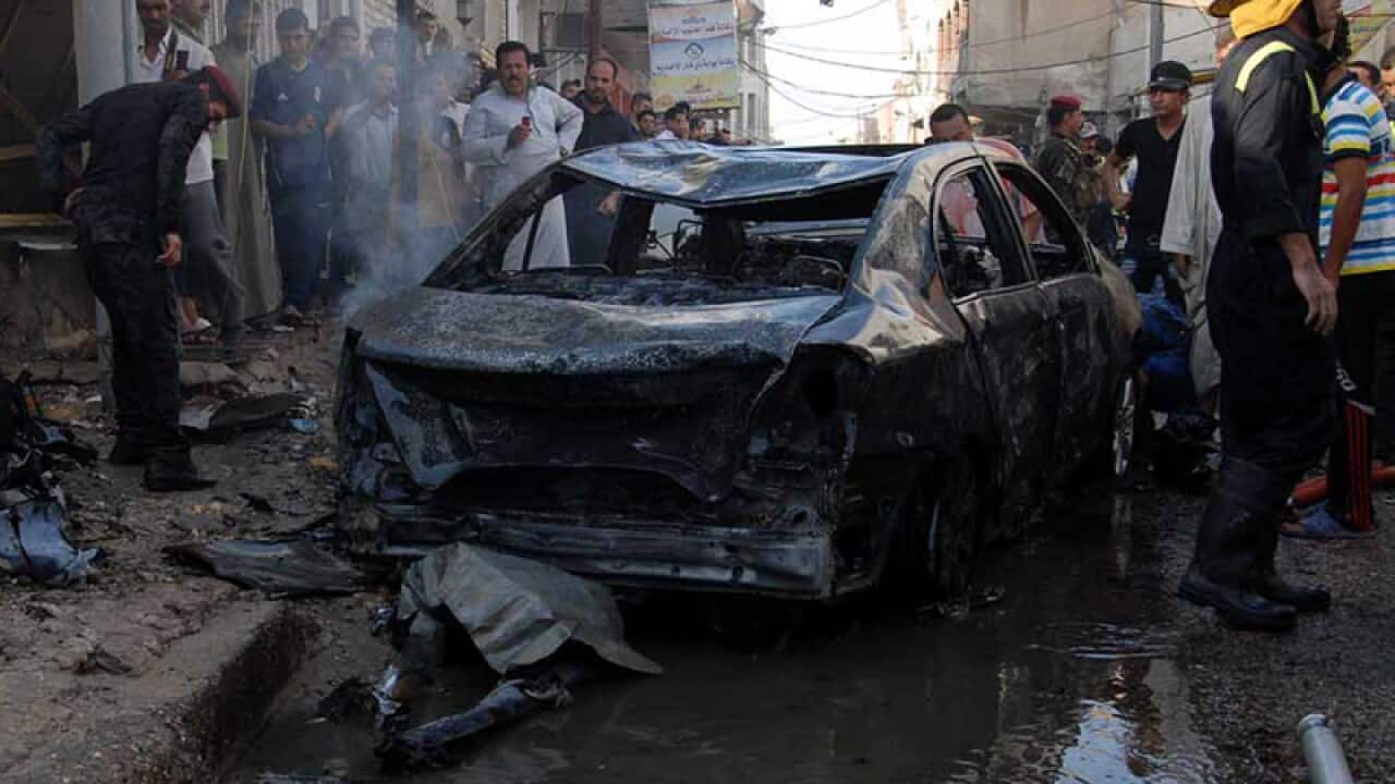 Iraqis gather near the remains of a vehicle at the scene of a car bomb