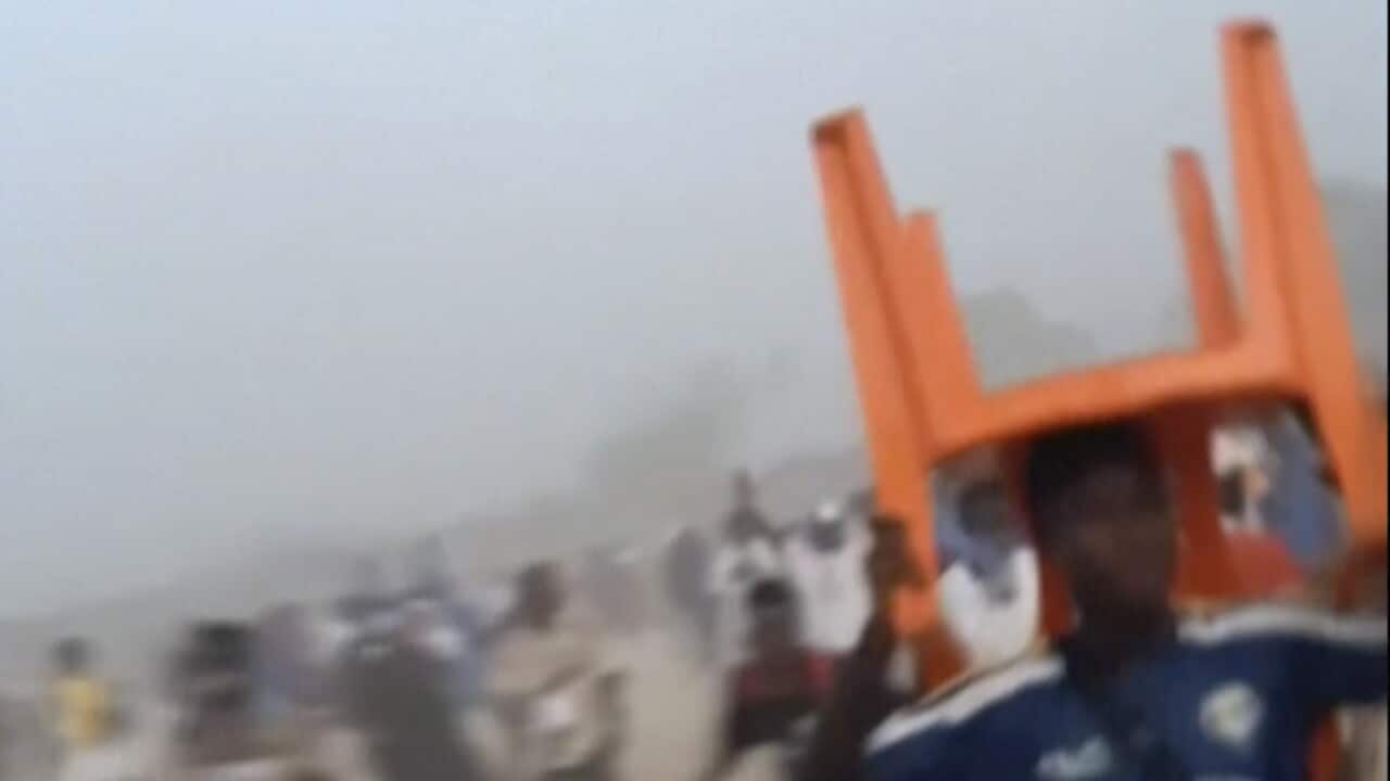 A man in a football jersey holds a chair above his head while running.
