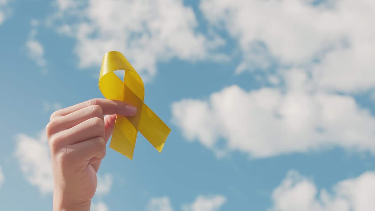 Hand holding a yellow endometriosis awareness ribbon over blue sky