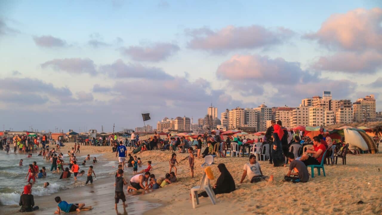 A crowd of adults and children on the beach during sunset, with the city skyline in the background.