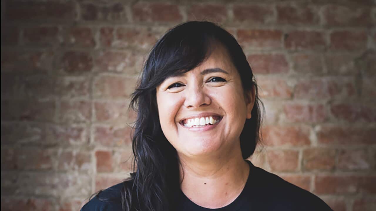 A woman is smiling while standing in front of a brick wall.