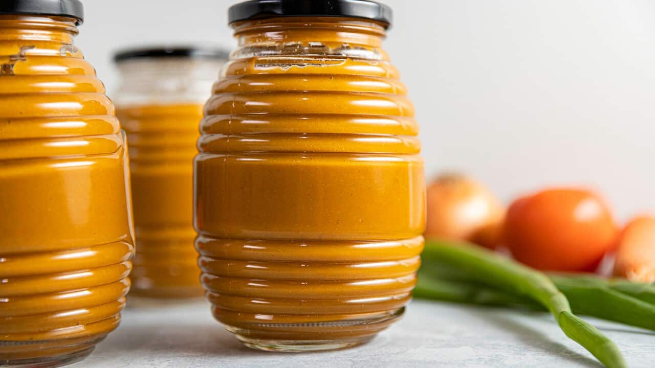 Three interesting glass jars with with a grooved pattern around the circumerence and black lids are filled with an orange sauce.