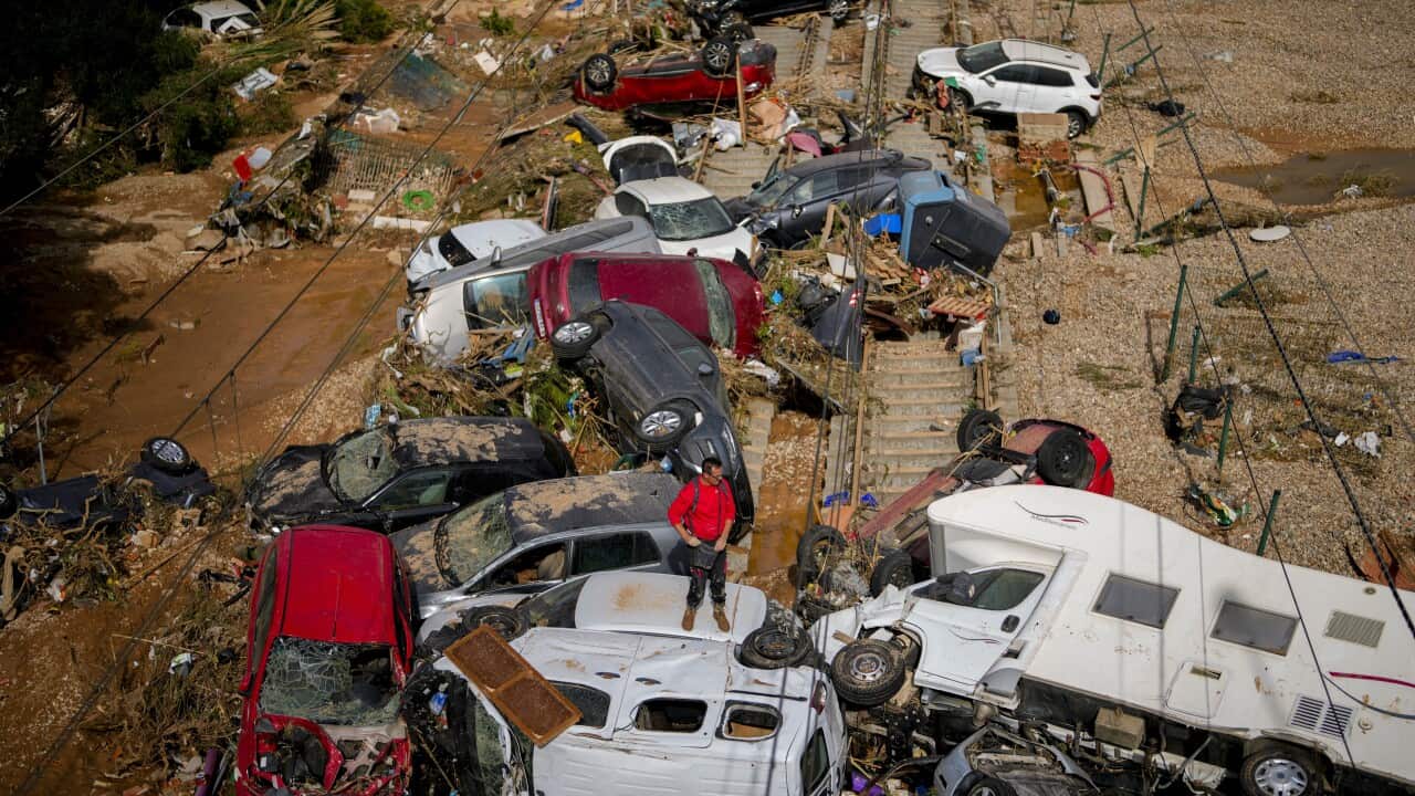 A person in a red jacket stands on the wreckages of cars strewn across a railway line