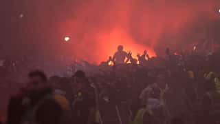 Fans at Federation Square seen in silhouette amongst red flare smoke