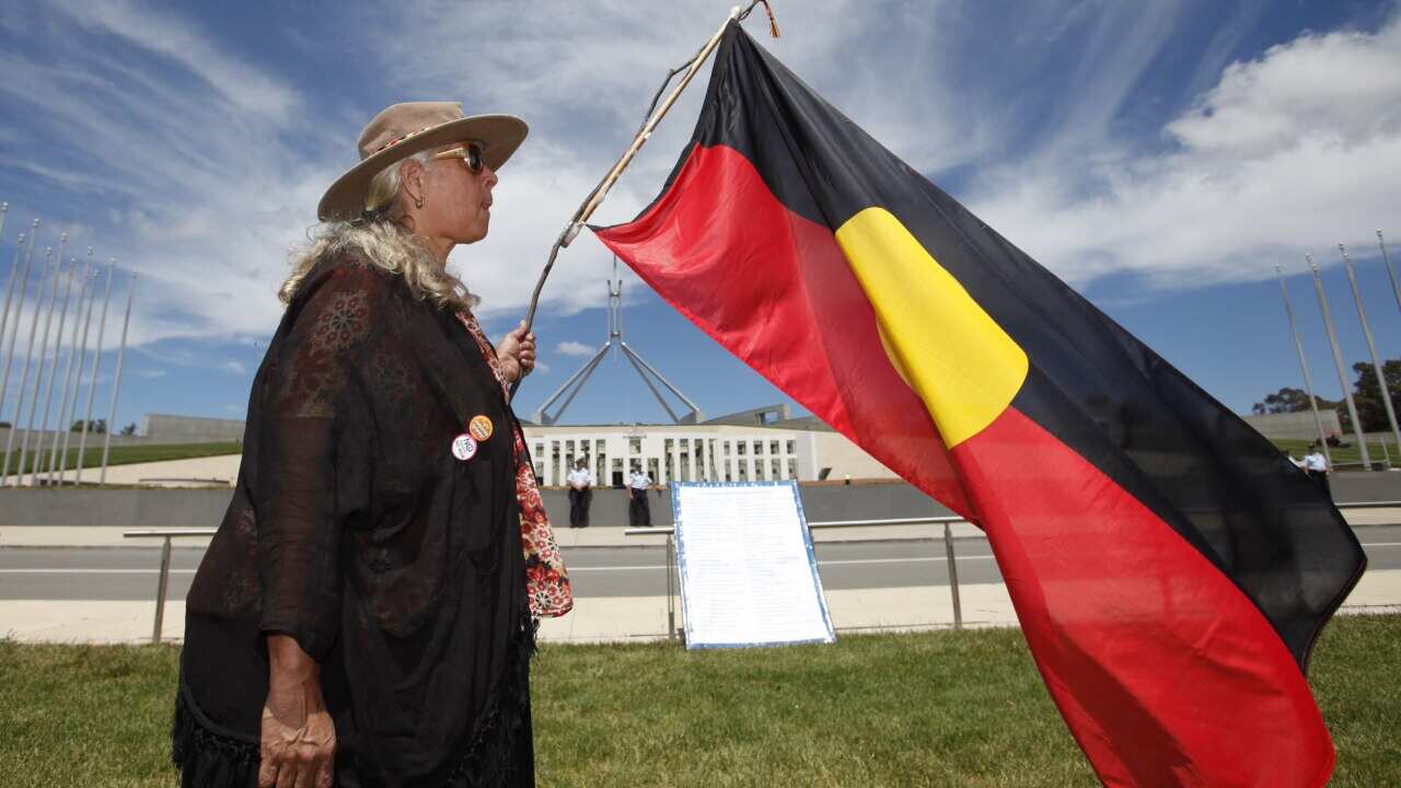A woman holds an Australian Aboriginal flag in front of the Parliament House in Canberra