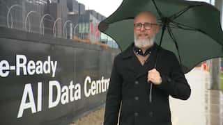 A man walking in front of a data centre holding an umbrella.