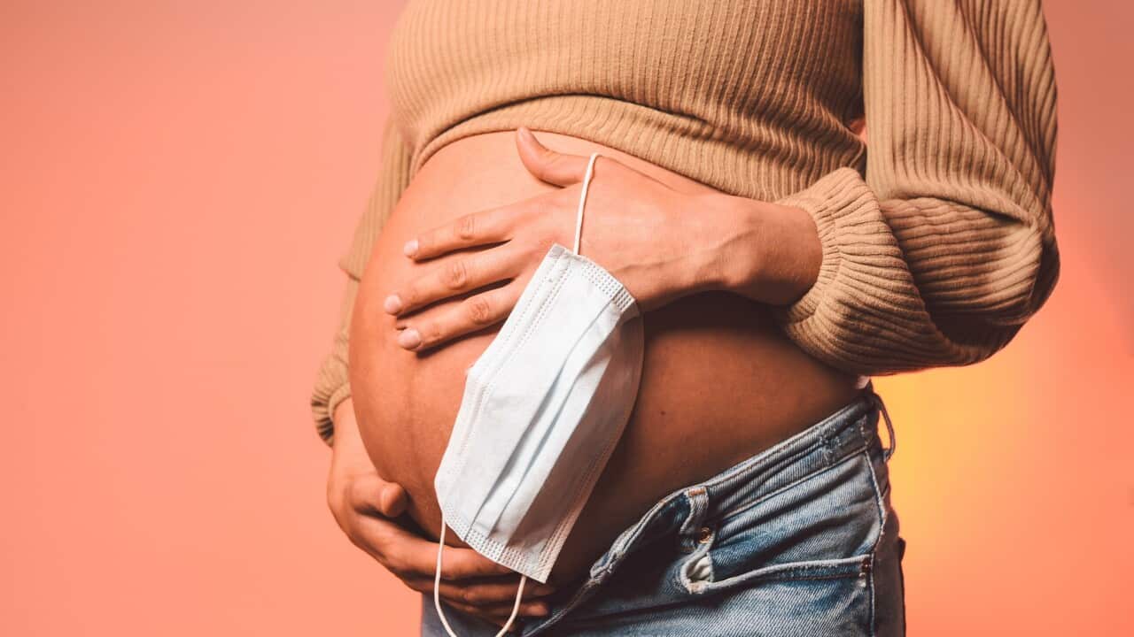 A pregnant woman holds a face mask.