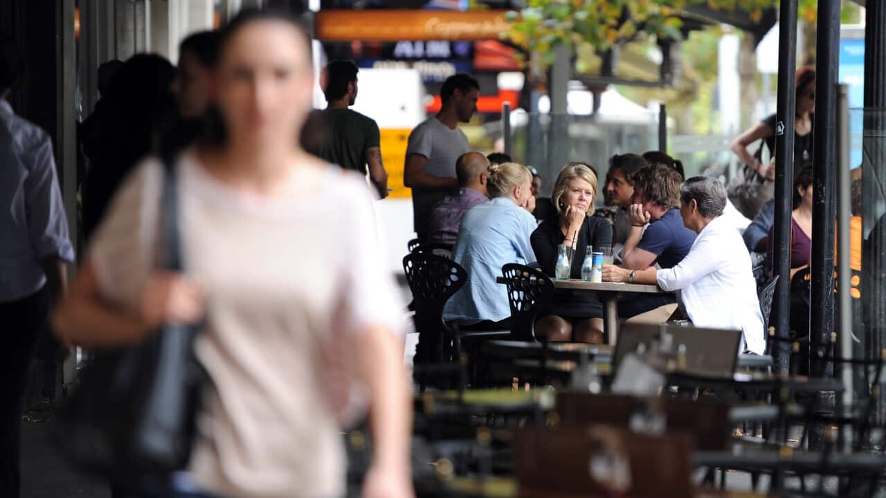 People sitting on the footpath outside cafes in Lygon Street in Carlton.