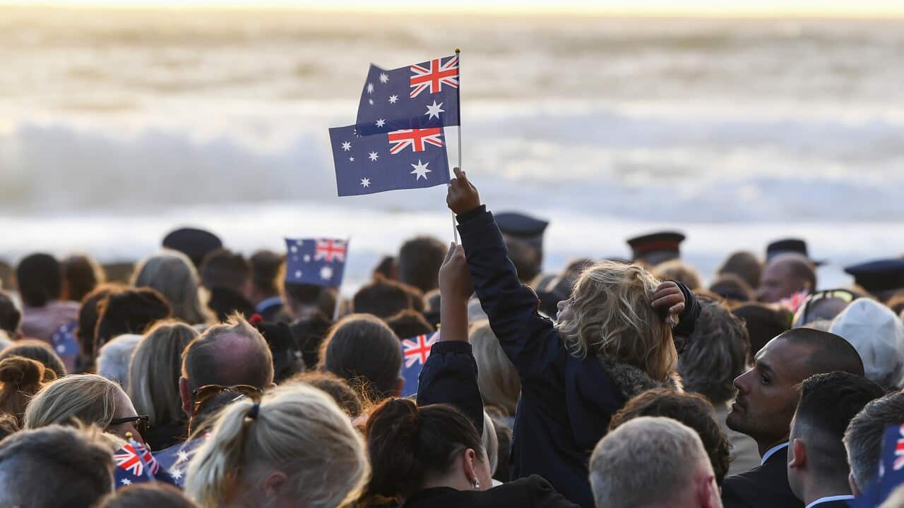 Rear view of a group of people facing the surf. Some are holding small flags up